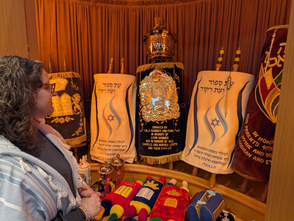 photo - Rabbi Susan Tendler at Beth Tikvah’s aron hakodesh, where two Torahs feature covers memorializing heroes lost in the latest war